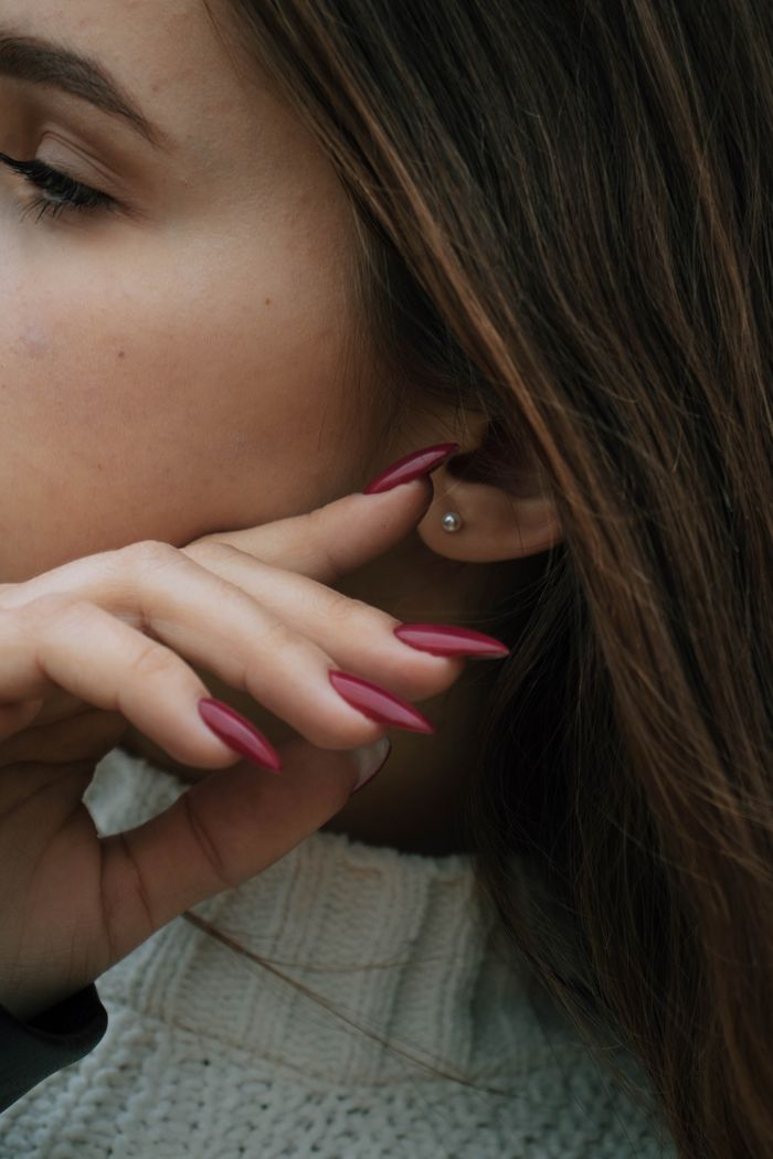 Detailed close-up of a woman with pearl earring and painted red nails, showcasing elegant jewelry.