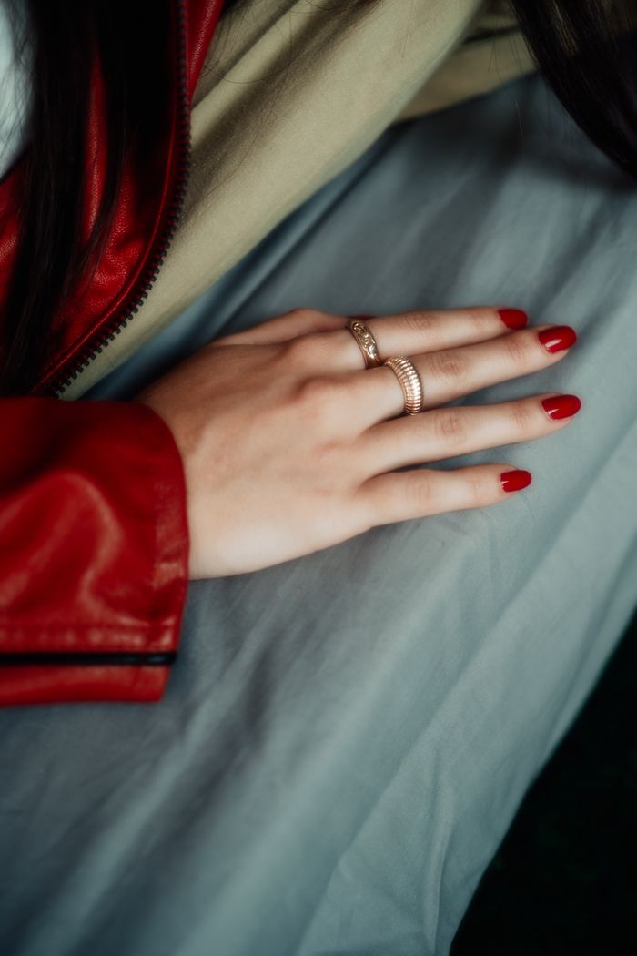 Close-up of a hand with red manicured nails and rings, lying on fabric.