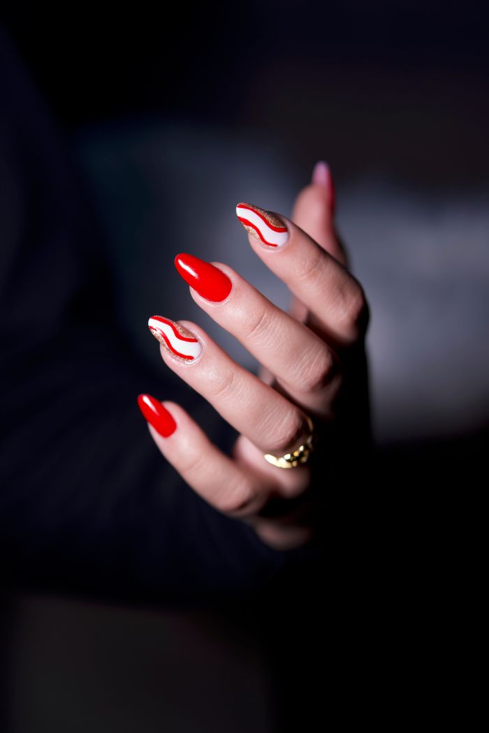 Close-up of a hand with vibrant red manicure and artistic designs, showcasing elegance and style.