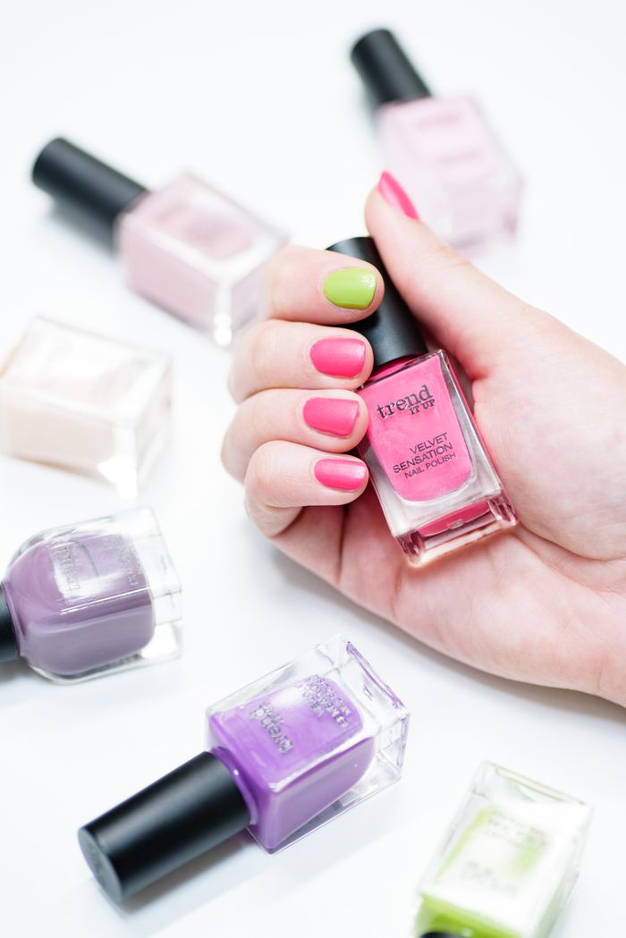 Hand holding diverse nail polish bottles in vibrant colors on white background.